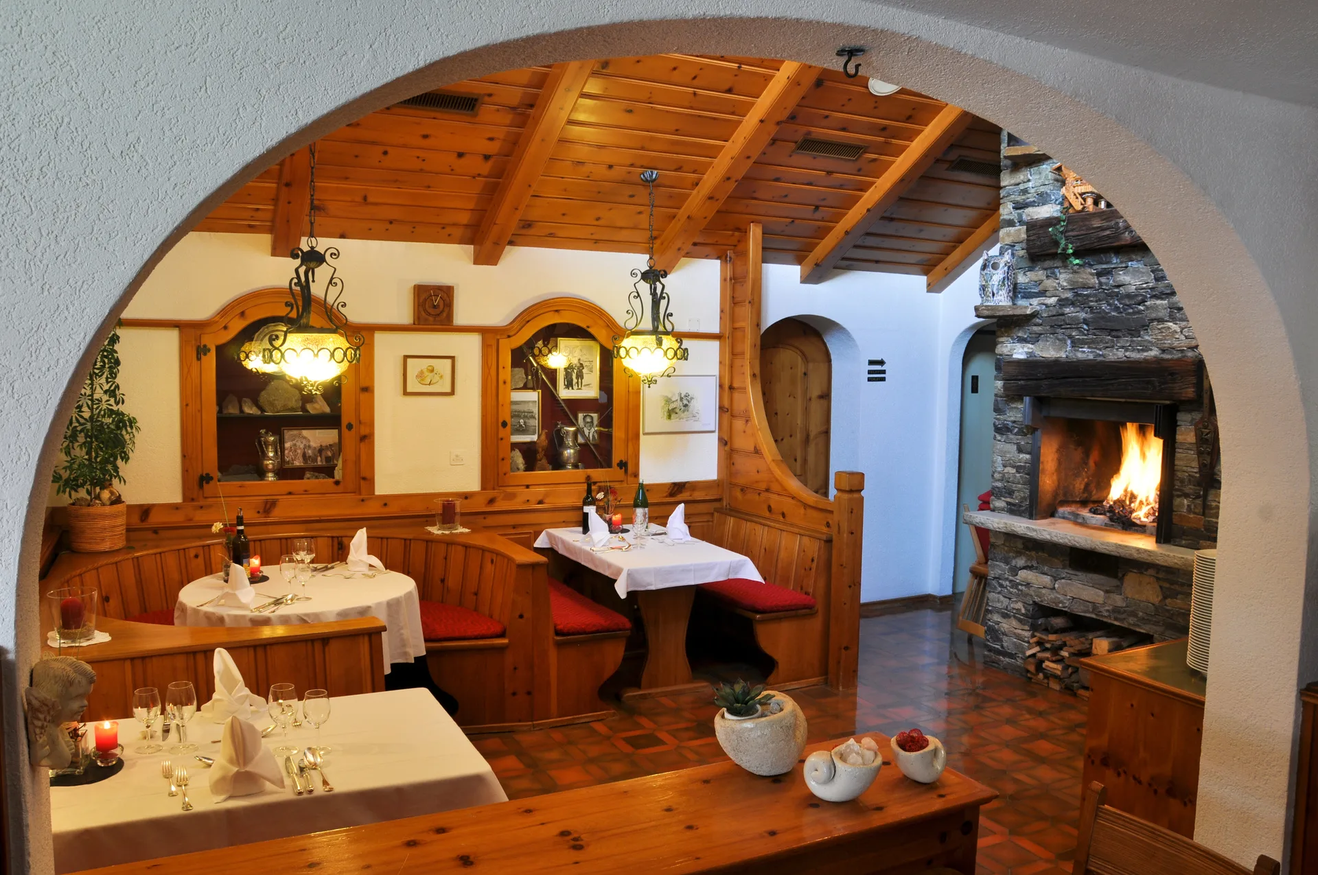 Restaurant-Stübli mit Holznischen, weissen Tischdecken und loderndem Cheminée